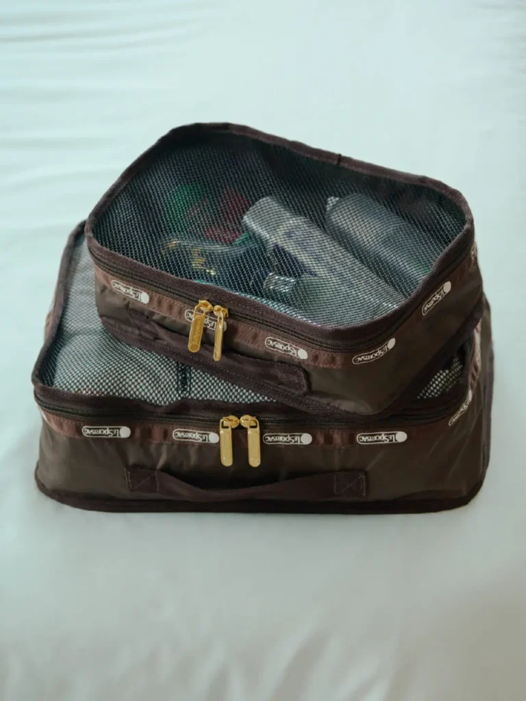 Brown LeSportsac mesh packing cubes stacked together, revealing neatly organized travel essentials through breathable zippered panel