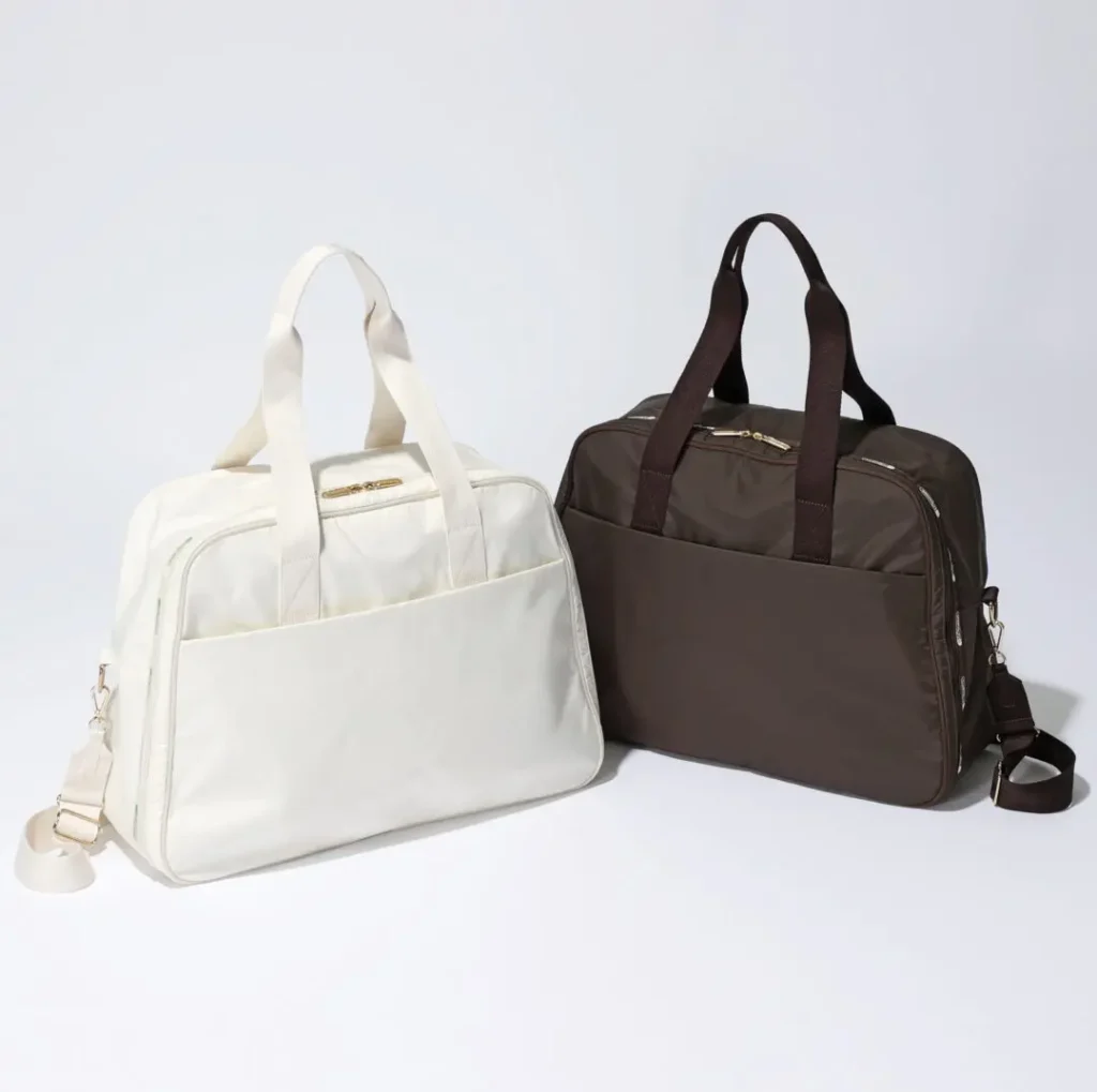 White and brown LeSportsac duffel bags with dual carry handles and detachable shoulder straps presented against a clean studio backdrop