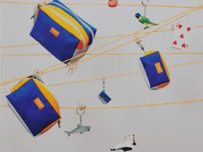 STANDARD SUPPLY x bPr BEAMS 50th anniversary campaign featuring three blue, orange, and silver utility pouches suspended on cords alongside playful keychains, a toy bird, playing cards, and miniature accessory