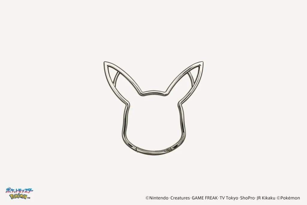 Silver metal key ring shaped like Pikachu's head silhouette with pointed ears, photographed against a clean white background as part of a Pokémon leather accessories collection