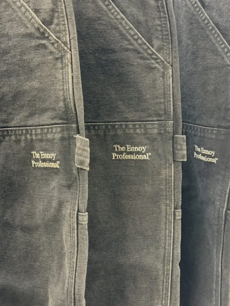 Detailed view of washed black carpenter shorts featuring oversized utility pockets, hammer loop, contrast fading, and white embroidered "The Ennoy Professional" logo on the front pocketDetailed view of washed black carpenter shorts featuring oversized utility pockets, hammer loop, contrast fading, and white embroidered "The Ennoy Professional" logo on the front pocket