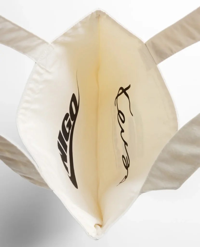 Interior view of a natural canvas tote bag showing the reverse sides of the Nike x NIGO and Kenzo logo prints with stitched seams and open construction