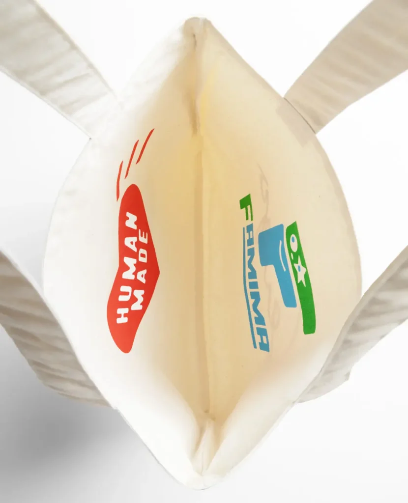 Interior view of a canvas tote bag featuring the Human Made heart logo on one side and the colorful Famima logo on the opposite side with reinforced stitch