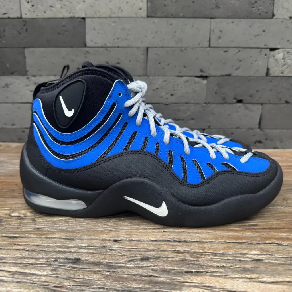 Side profile of the Nike Air Bakin in black and royal blue, highlighting the sculpted midsole, visible Air unit, white Swoosh, and signature flowing upper overlay