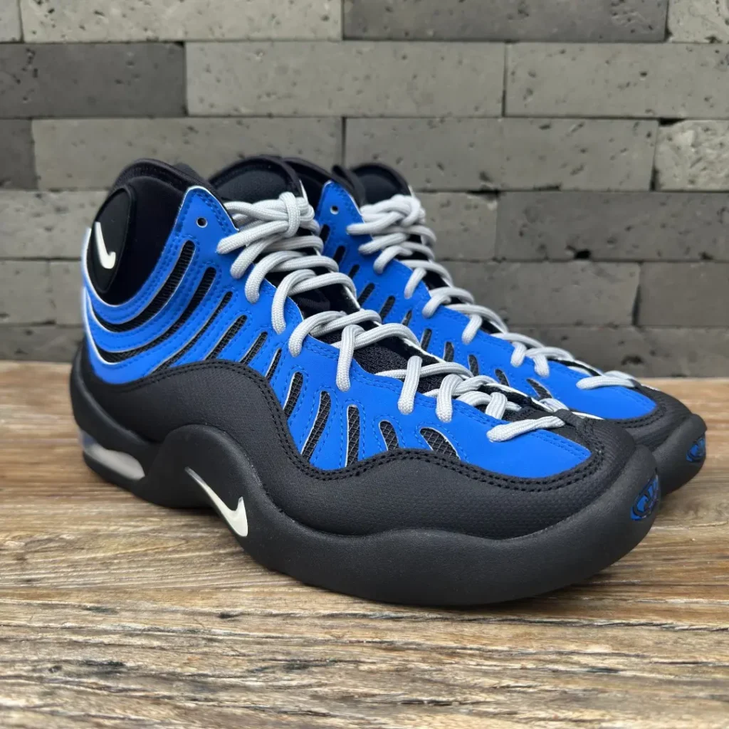 Three-quarter front view of the Nike Air Bakin showcasing the black and royal blue upper, light gray laces, rounded toe, and visible Air cushion