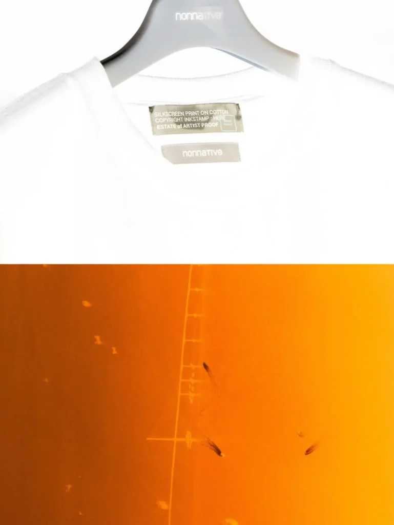 Detail of the white nonnative collaboration T-shirt collar and printed neck label, paired with an orange abstract photographic background