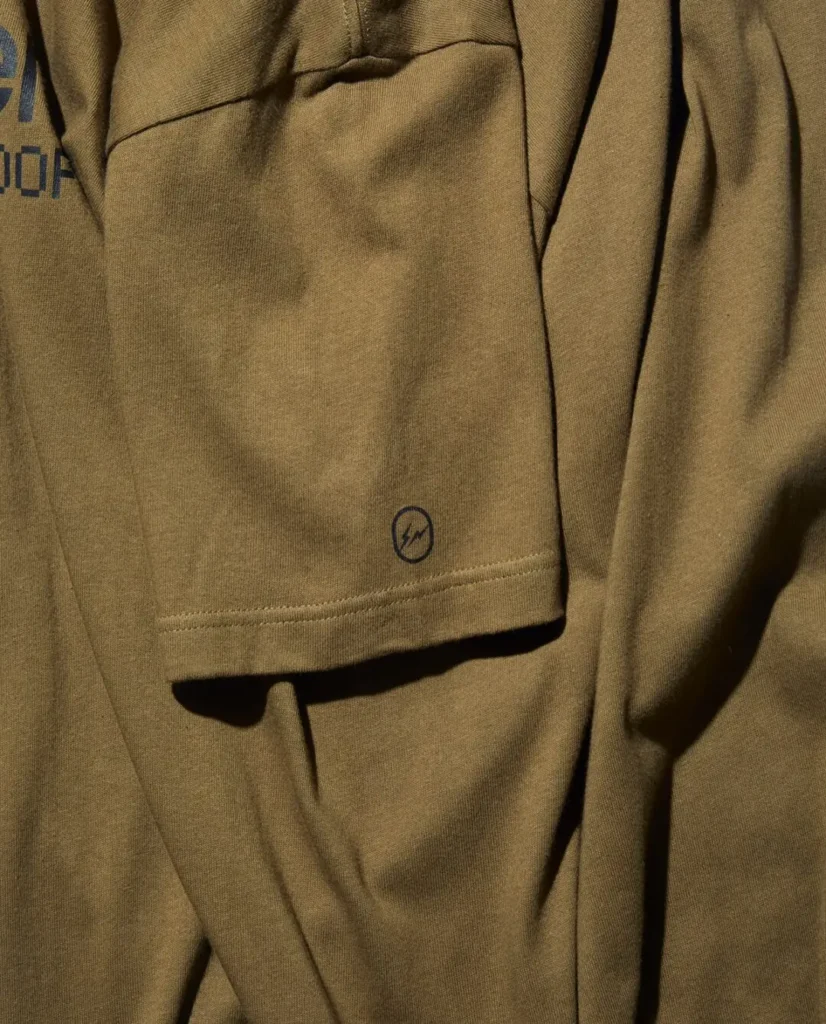 Close-up of the olive green Tee sleeve showing the Fragment Design lightning bolt logo printed near the cuff