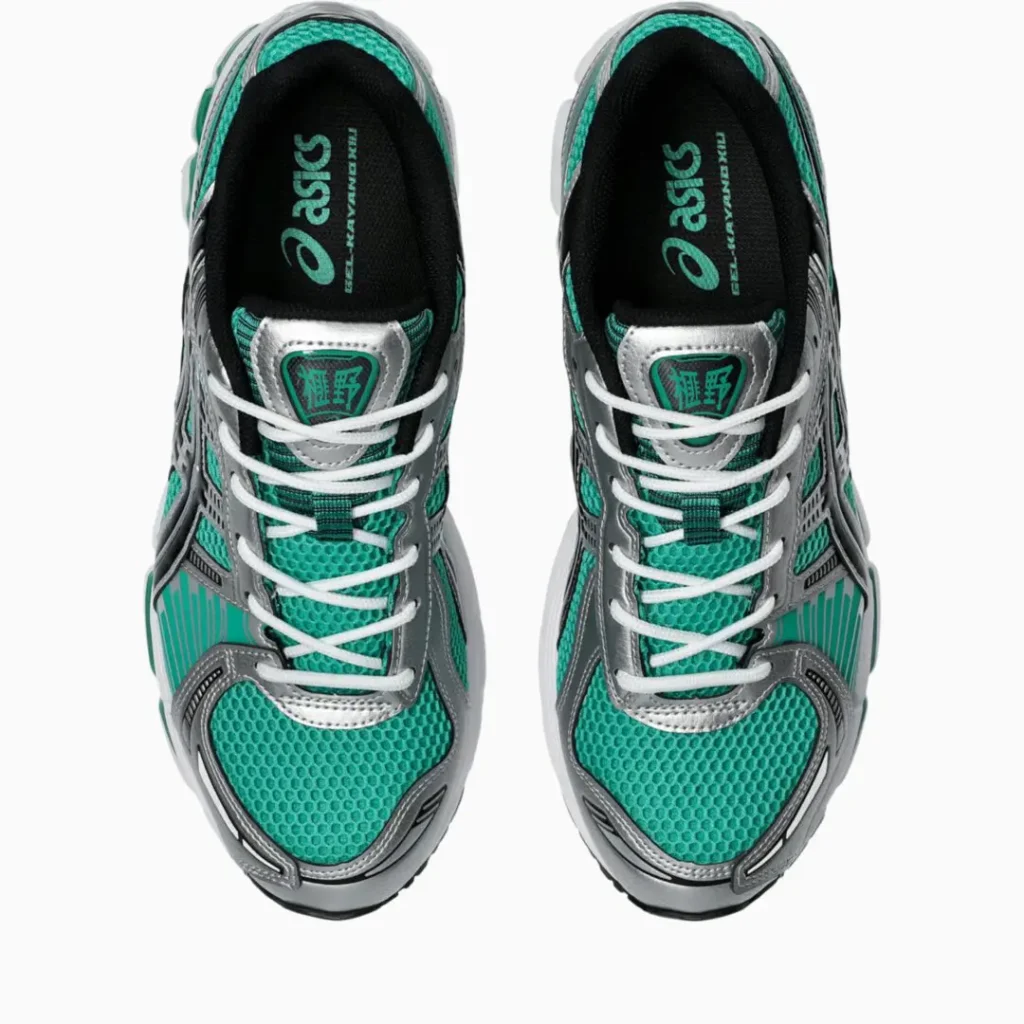 Top-down view of the ASICS GEL-KAYANO 14 showing teal honeycomb mesh, metallic silver overlays, white laces, black sockliners with ASICS branding, and tongue labels with green graphic detail