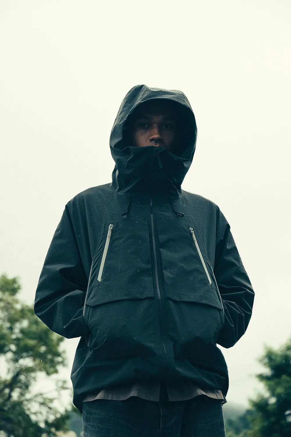 Model wearing a black technical waterproof hooded jacket outdoors in rainy conditions