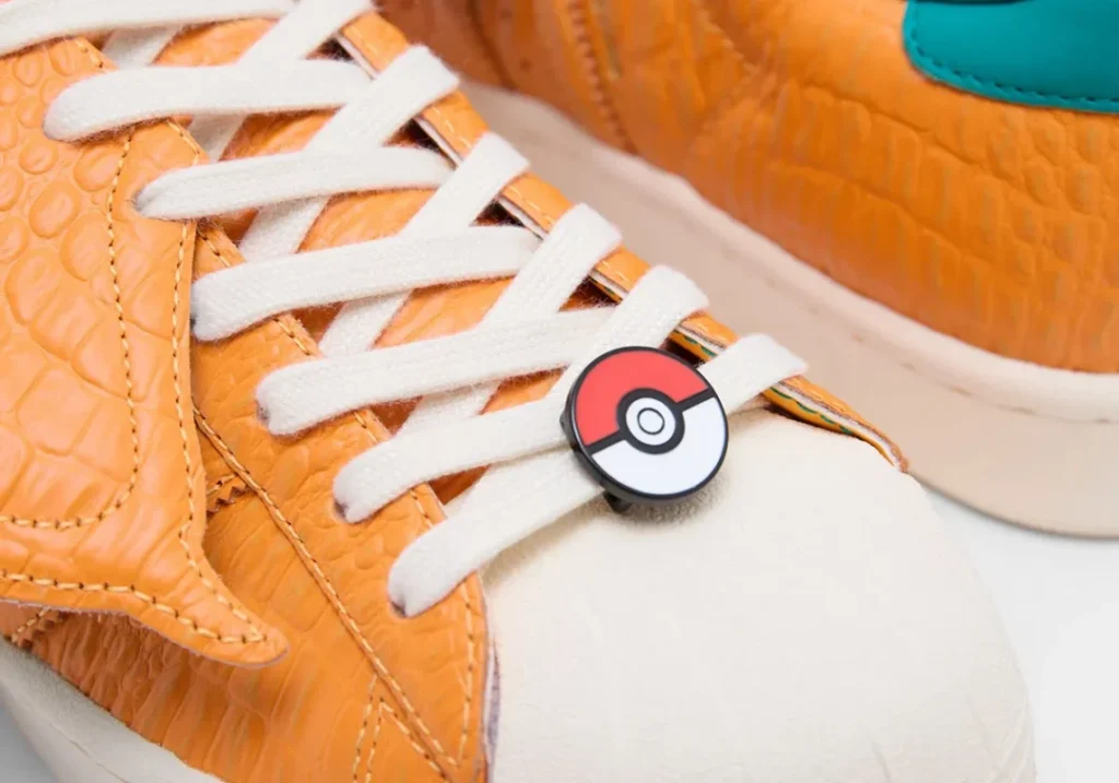 Close-up of the Charizard-inspired shoe featuring white laces, orange reptile-textured leather, and a Poké Ball lace accessor