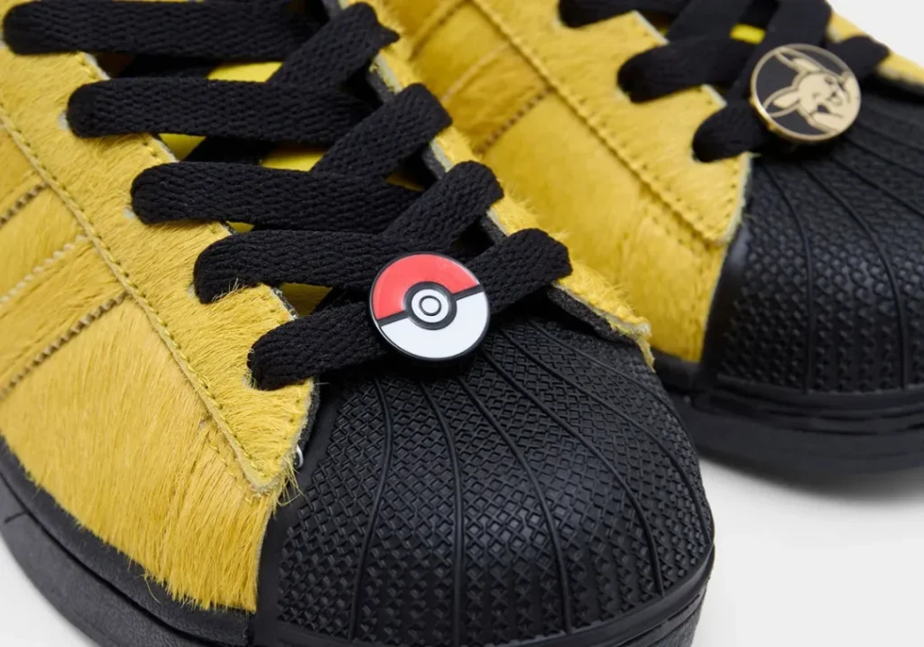Close-up of the Pikachu Superstar Mid showing black shell toe texture, black laces, and a Poké Ball lace jewel