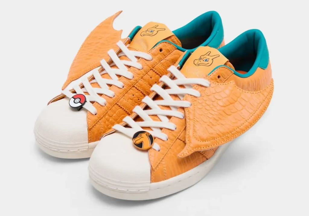 Pair of orange adidas sneakers with reptile-textured leather, wing-shaped side panels, teal lining, and Charizard-themed brand