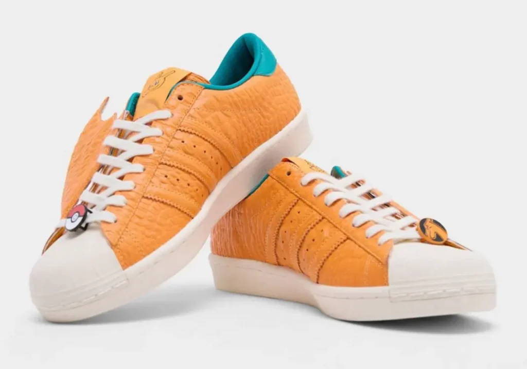 Angled view of the Charizard-inspired adidas sneakers highlighting textured orange uppers, white shell toes, and sculpted wing overlay