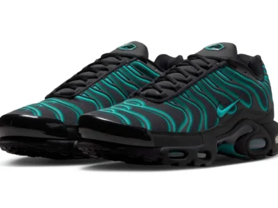 A pair of Nike Air Max Plus shoe in black with vibrant teal gradient TPU wave overlays is shown from a front three-quarter angle. The shoes feature glossy black mudguards, black laces, teal Swooshes, Tuned Air cushioning, and a clean white studio background