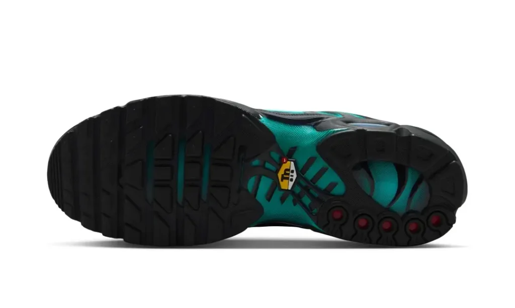 The outsole of the Nike Air Max Plus reveals a predominantly black rubber tread with teal midfoot detailing, view Tuned Air shank branding, circular traction pods, and red rubber accents beneath the forefoot