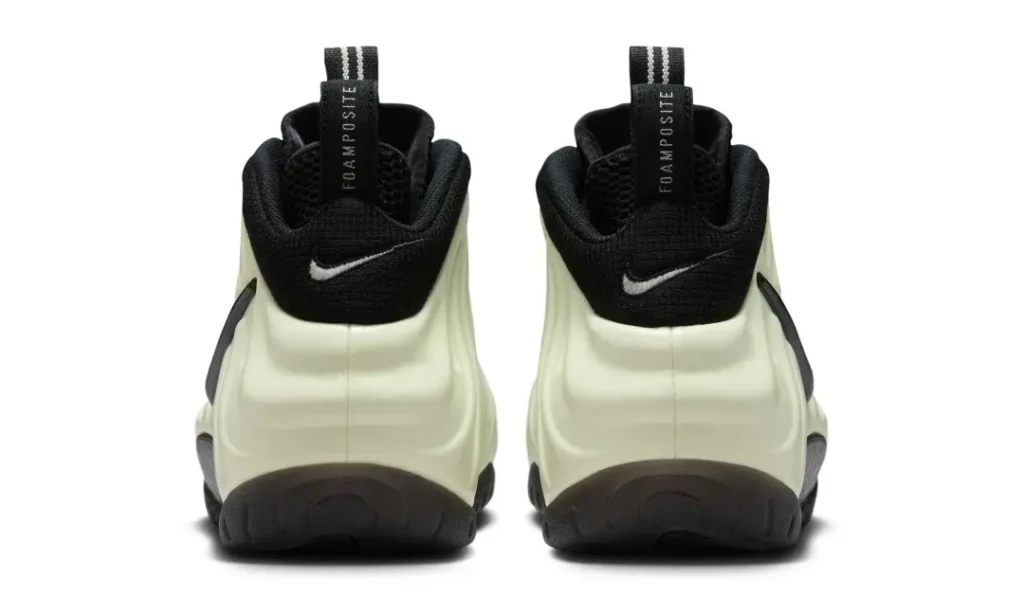 Rear view of a pair of Nike Air Foamposite shoe showing the heels. Both shoes display "FOAMPOSITE" text on the pull tabs, black Nike swooshes, and the sculpted heel design against a white background
