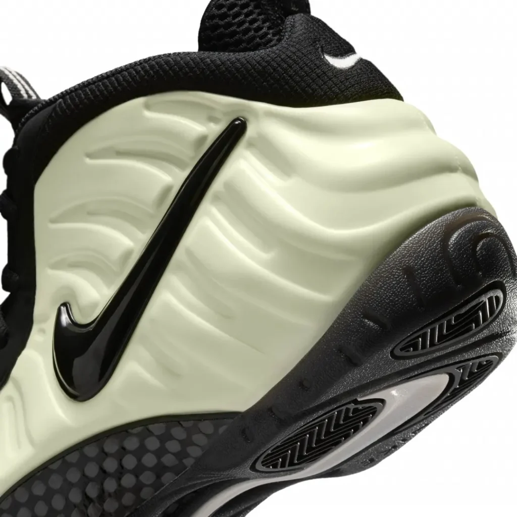 Close-up of the heel and midsole area of a Nike Air Foamposite sneaker, showcasing the glossy black swoosh, textured foam material, and detailed black outsole with grip pattern