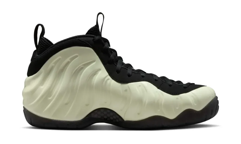 Side profile of a Nike Air Foamposite Pro sneaker in black and cream on a white background. The image beautifully captures the futuristic wavy Foamposite design and sleek sil