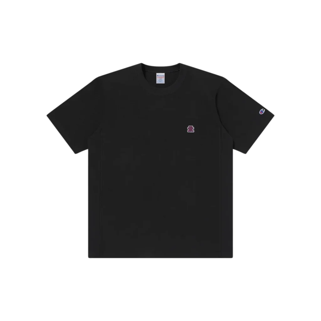 Front product image of the black Champion x The Black Eye Patch short sleeve Tee featuring a small embroidered chest logo and Champion sleeve embroidery on a plain white background