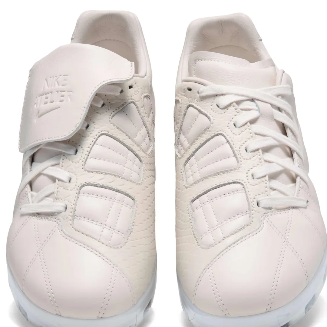 Front view of the Nike Total 90 football shoes in an all white colorway, shown side by side. The left shoe features the signature fold-over tongue with embossed Nike Total 90 branding, while both shoes display quilted leather panels, white laces, and a matching white sole.