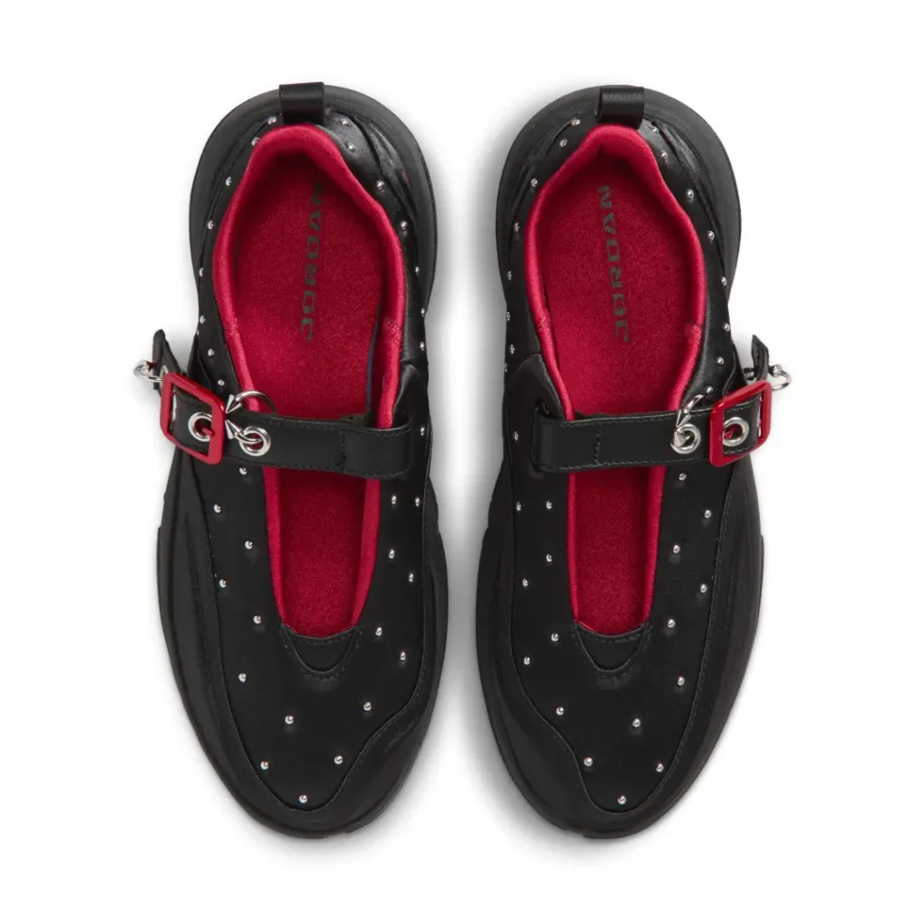 Top-down view of the pair reveals black studded uppers, oversized adjustable straps with red buckles and silver hardware, plush crimson lining, and matching red insoles with Jordan brand