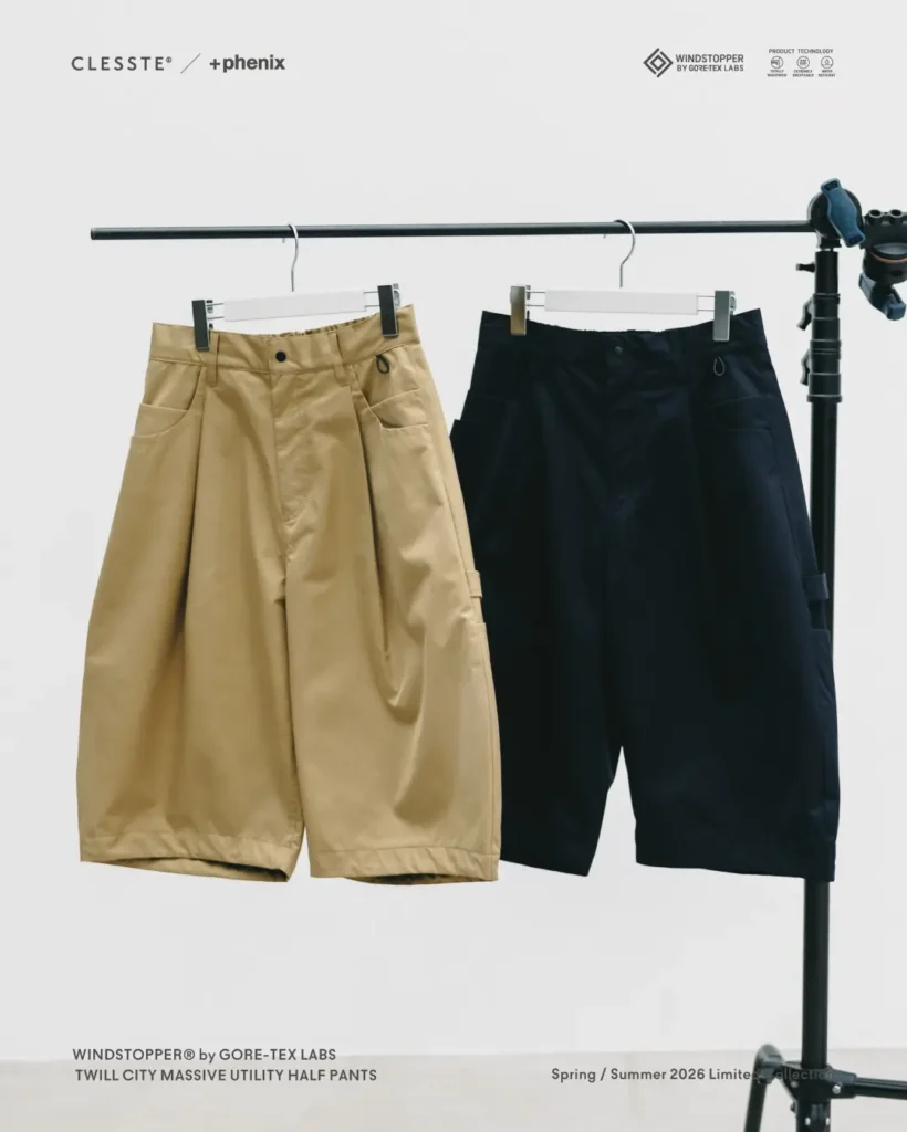 lack and khaki CLESSTE × +phenix utility half pants hanging side by side on a rack, showcasing oversized tailoring and technical outdoor construction