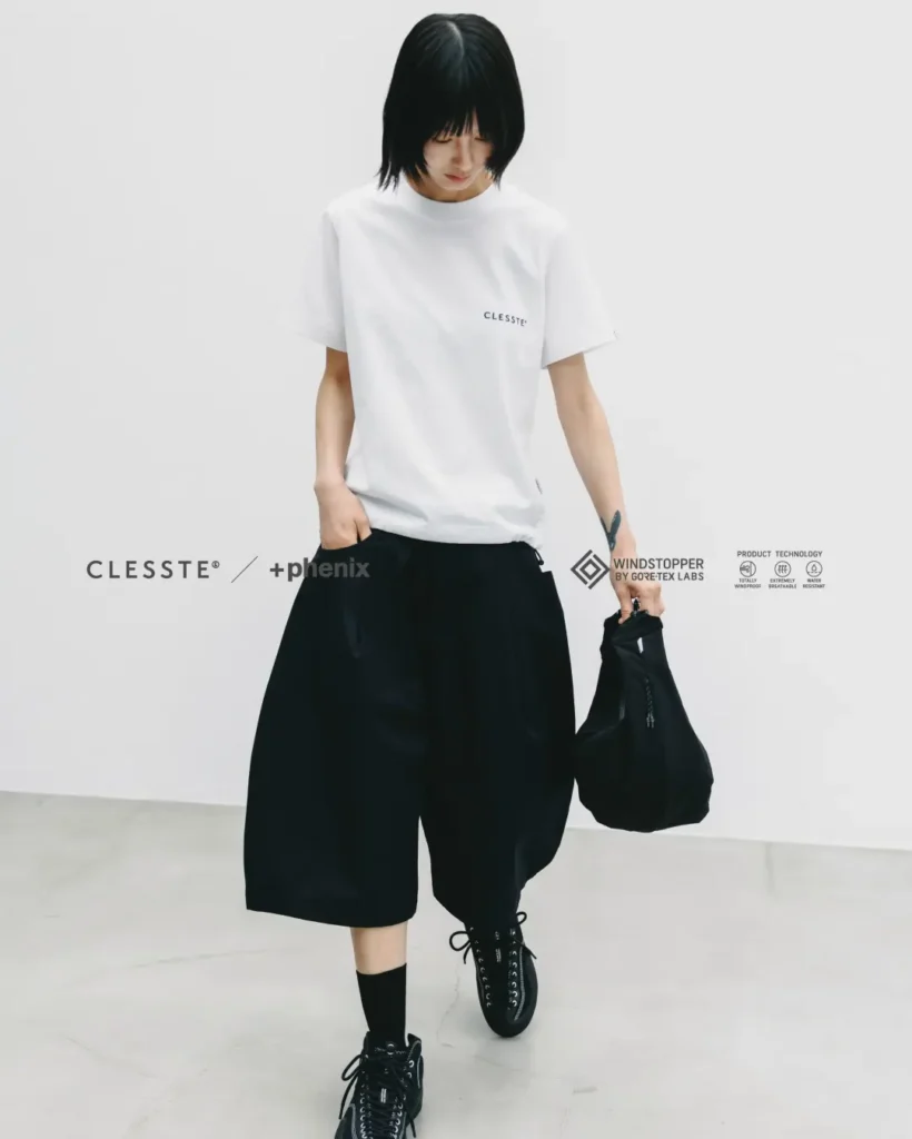Female model wearing the black oversized WINDSTOPPER utility half pants with a white oversized T-shirt, black sneakers, and matching black carry bag