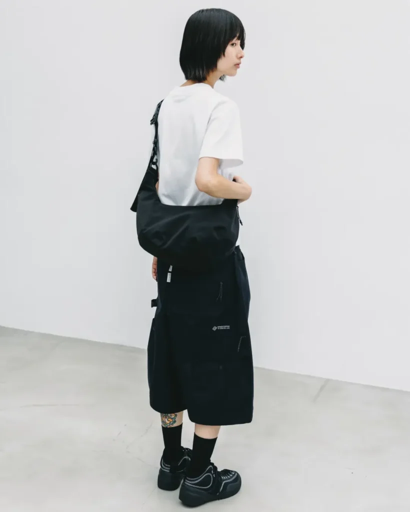 Side profile of a model wearing a white Tee, black technical balloon shorts, and a black crossbody bag, showcasing the relaxed silhouette and oversized utility style