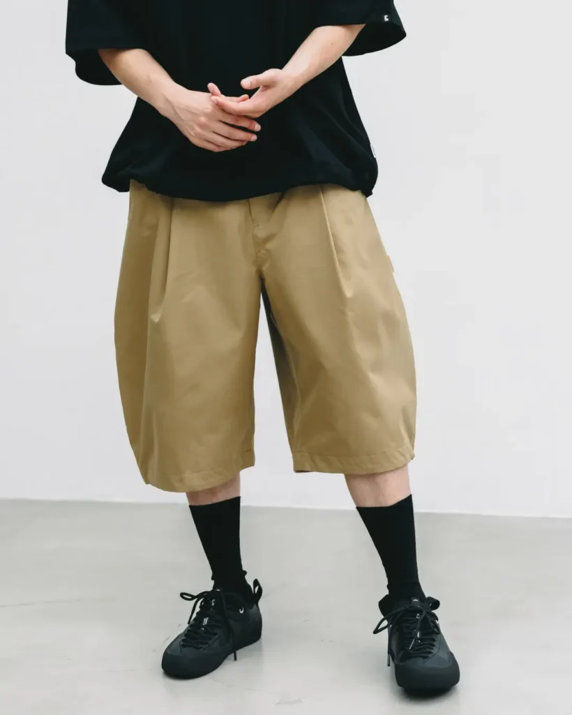 Cropped front detail of khaki oversized balloon shorts paired with an oversized black T-shirt, emphasizing the wide-leg shape, technical fabric, and minimalist style