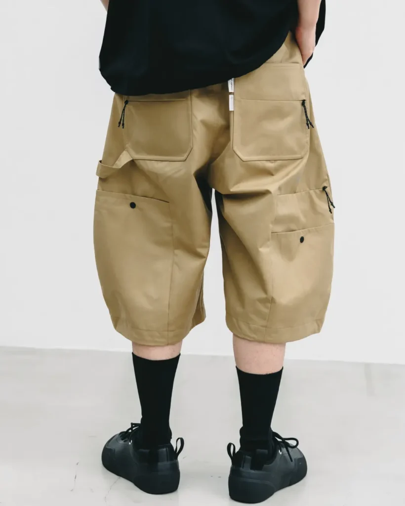 Rear view of khaki technical balloon shorts showcasing oversized patch pockets, utility loops, zippered storage, and structured construction with black socks and black shoe
