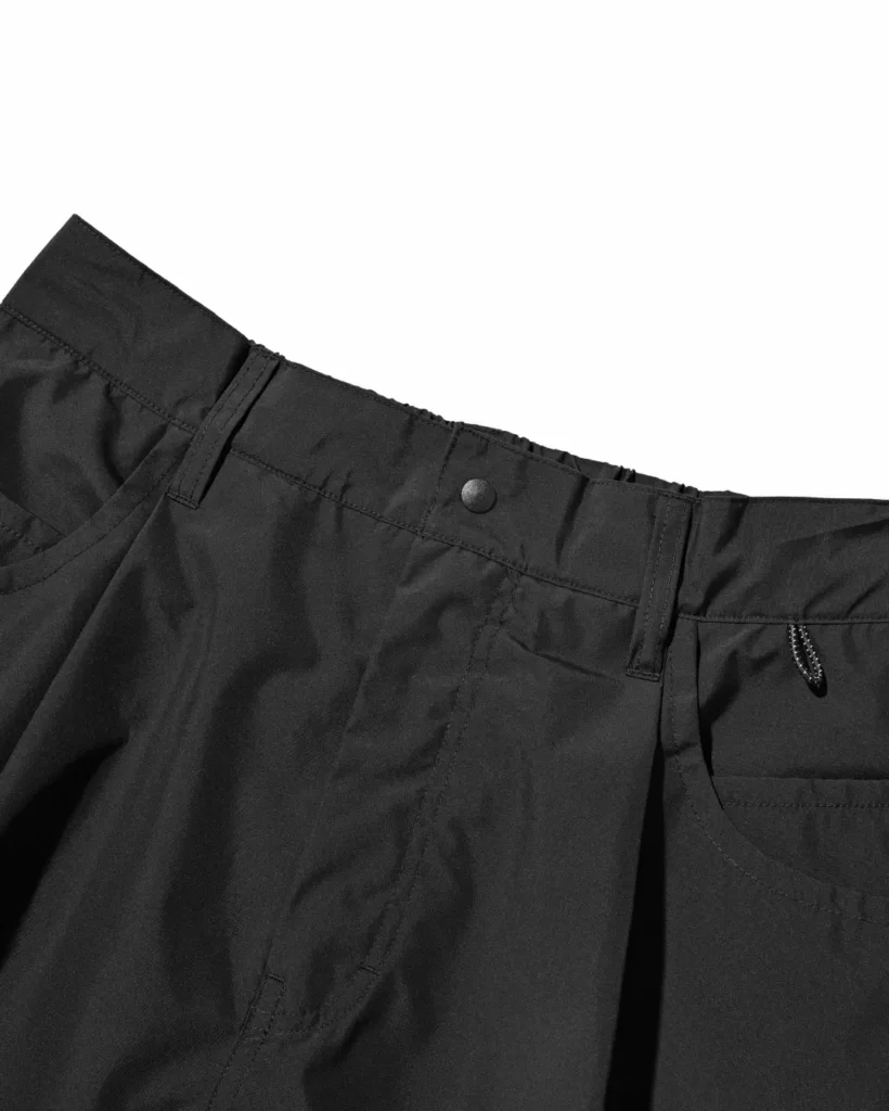 Close-up of the black utility half pants waistband featuring belt loops, snap-button closure, front fly, and reinforced stitching detail