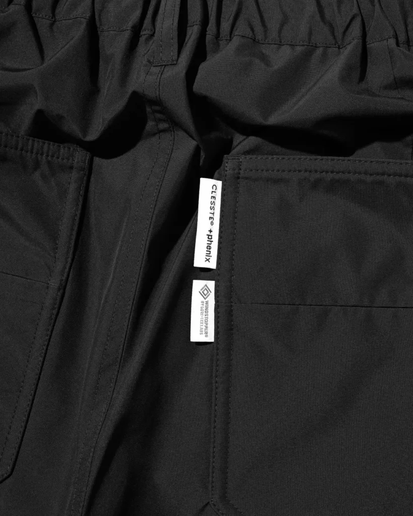Close-up of the black utility half pants waistband featuring belt loops, snap-button closure, front fly, and reinforced stitching detail