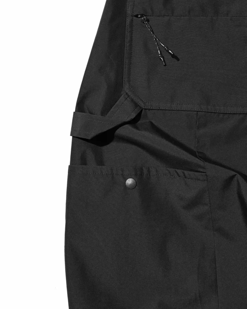 Close-up of the rear utility pockets showing woven CLESSTE × +phenix branding tags and durable pocket construction on the black pant
