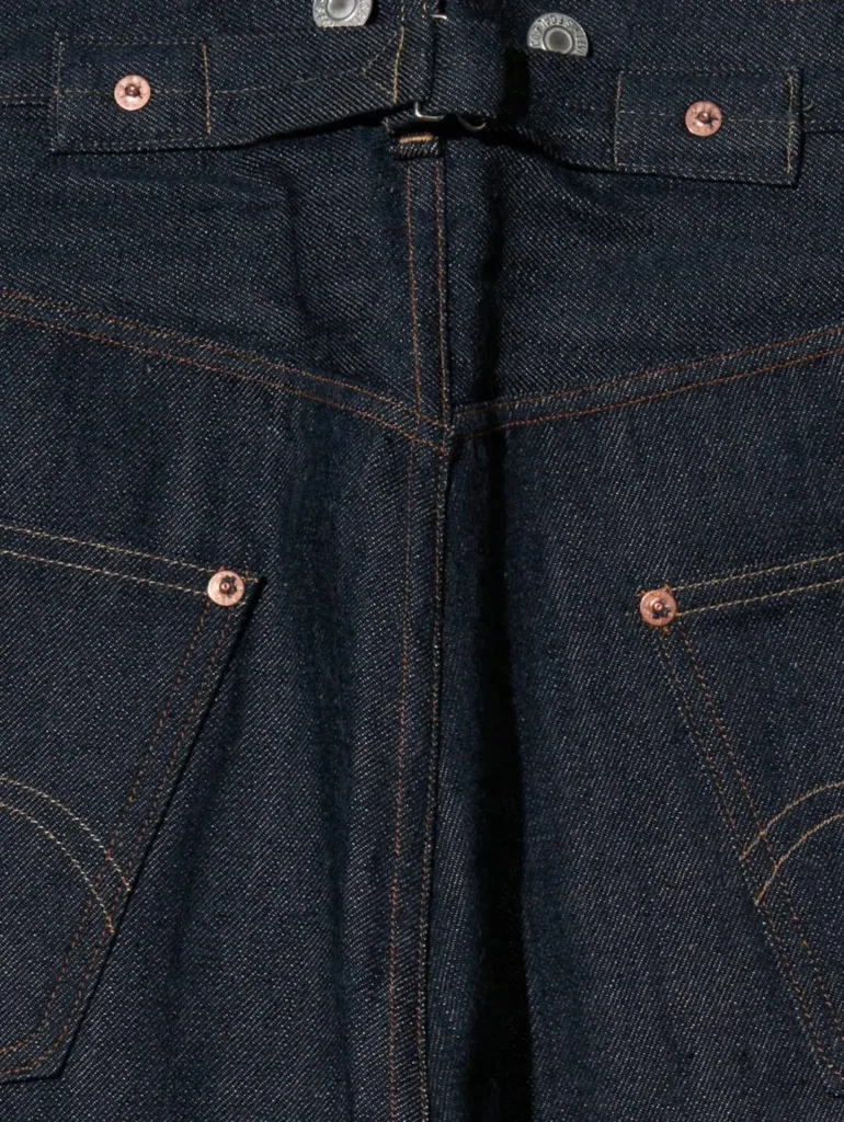 Detailed rear waist view highlighting the center back seam, hidden cinch-style waistband detail, contrast stitching, and upper back pocket construction on dark indigo denim