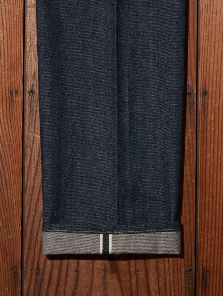 Close-up of the cuffed hem revealing the white-and-red selvedge ID along the folded edge of heavyweight dark indigo denim