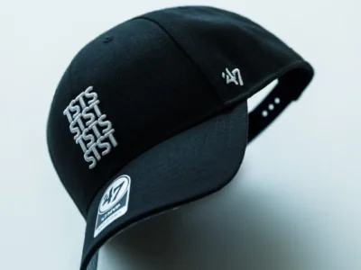Black 47 Brand adjustable baseball cap shown in an angled floating product view, featuring raised white TSTS embroidery on the front, a white '47 logo embroidered on the side, a curved brim, and a min black finish