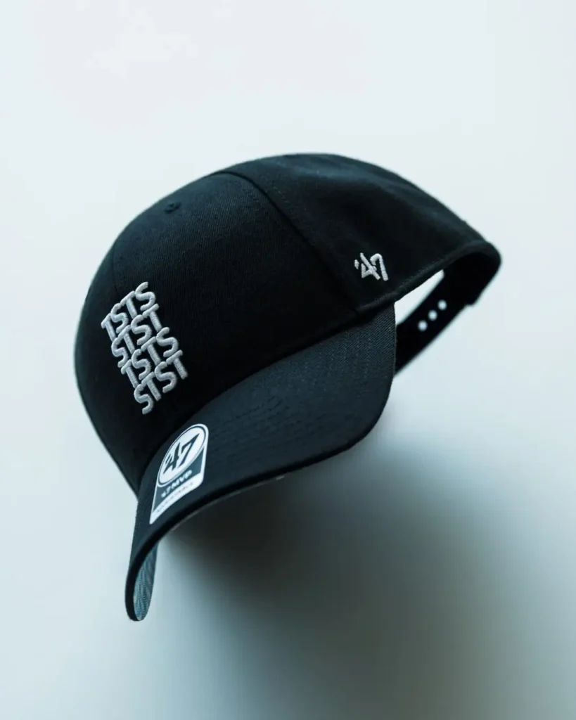 Black 47 Brand adjustable baseball cap shown in an angled floating product view, featuring raised white TSTS embroidery on the front, a white '47 logo embroidered on the side, a curved brim, and a min black finish