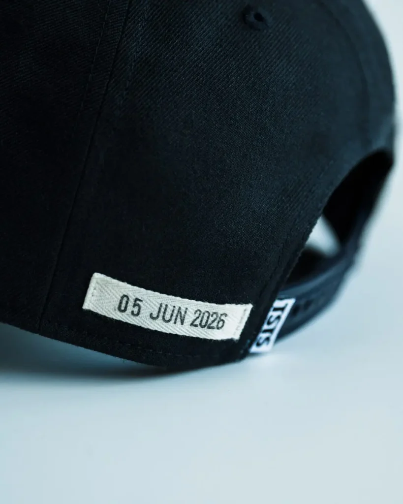 Rear close-up of the black adjustable cap showing a woven patch embroidered with the date "05 JUN 2025," the adjustable snapback closure, and a small woven TSTS label near the back open