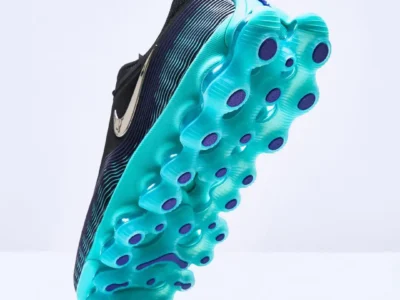 Bottom view of a black Nike Air Max shoe featuring a translucent aqua-blue Air unit outsole with deep circular traction pods accented in dark blue. The metallic silver Swoosh is visible along the side, highlighting the futuristic cushion system