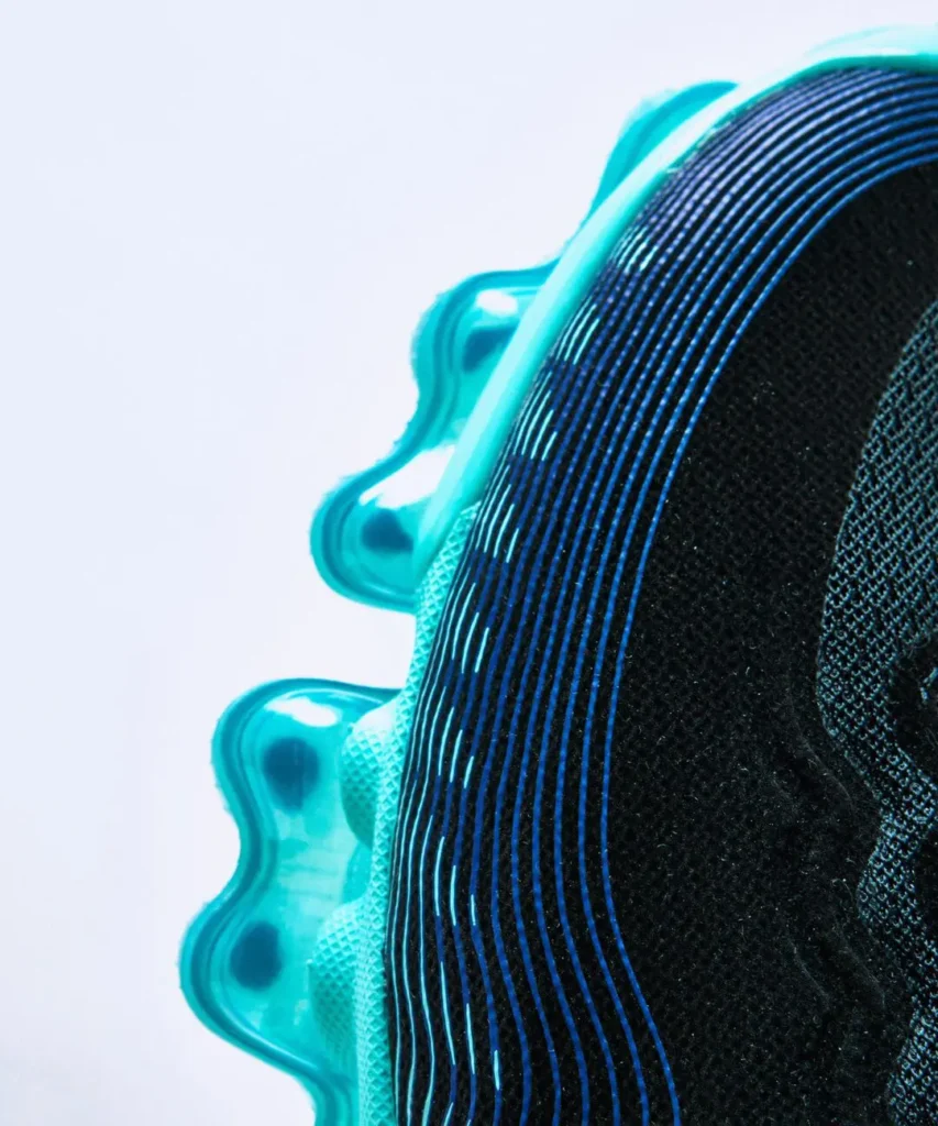 Close-up detail of the Nike Air Max upper showing fine blue gradient contour lines flowing across the black mesh side panel, with the translucent aqua-blue Air sole partially view in the background