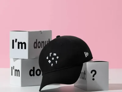 Black New Era "I'm Donut?" cotton dad cap displayed on white branded boxes with a soft pink backdrop, featuring white embroidered lettering on the crown and the classic New Era flag logo on the side