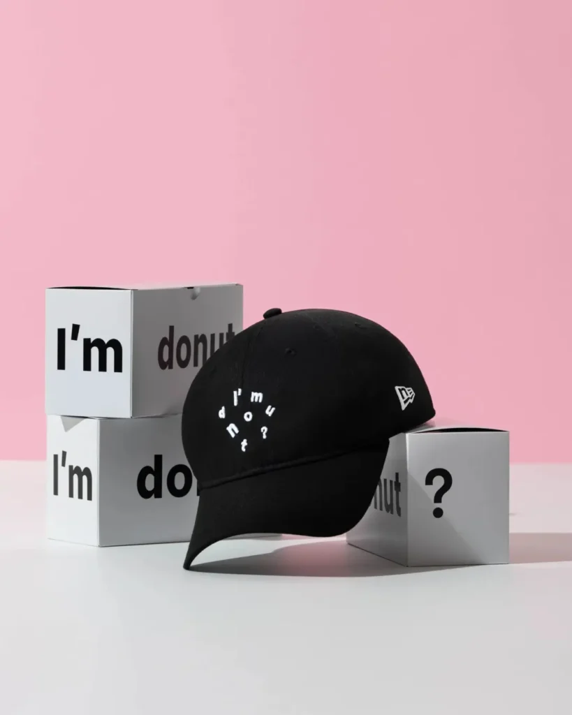 Black New Era "I'm Donut?" cotton dad cap displayed on white branded boxes with a soft pink backdrop, featuring white embroidered lettering on the crown and the classic New Era flag logo on the side