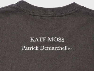 Close-up of the back neck print on the charcoal Tee, showing the white "KATE MOSS" and "Patrick Demarchelier" text centered beneath the collar