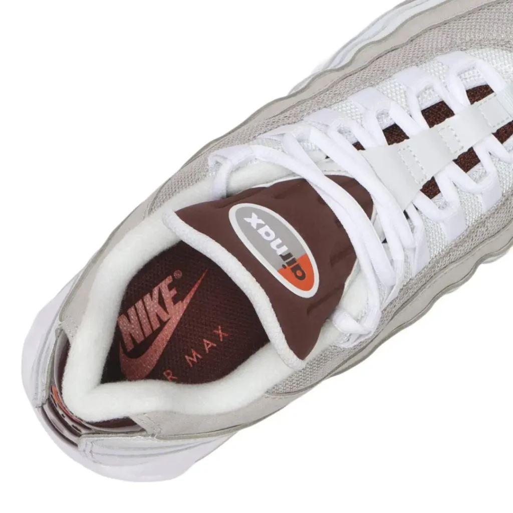 Angled overhead close-up of the Nike Air Max 95 emphasizing the padded brown Air Max tongue, white lace system, light grey mesh and suede upper, plush white collar lining, and brown Nike Air-branded insole