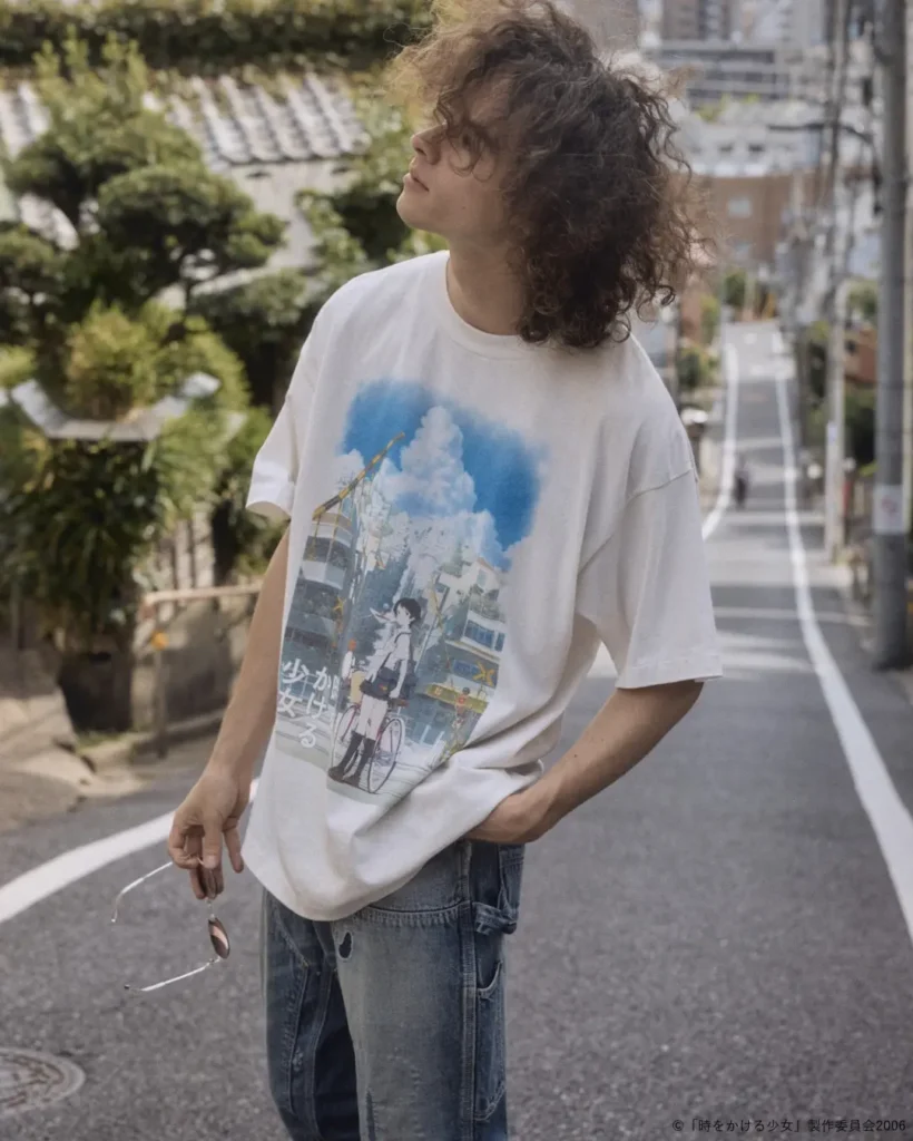 Model wearing an oversized white anime graphic T-shirt on a quiet hillside Tokyo street, holding sunglasses while showcasing the oversized fit and detailed front artwork