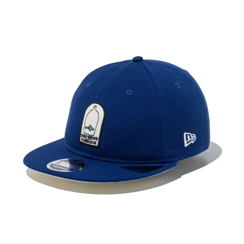 Royal blue flat brim cap with a bottle and fish embroidered patch on the front and white New Era logo on the side