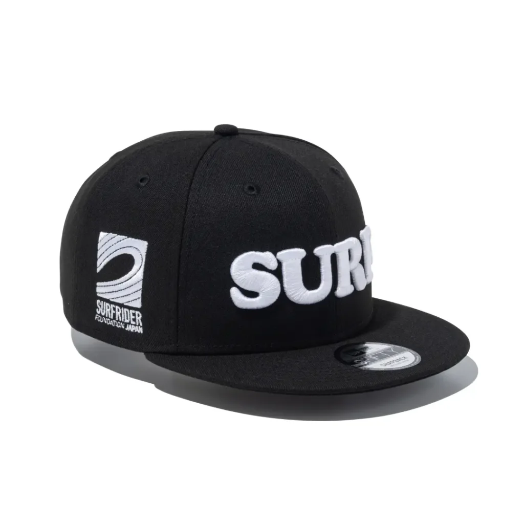 Black flat brim snapback cap with oversized white "SURF" embroidery across the front and Surf Rider Foundation Japan logo stitched on the side panel