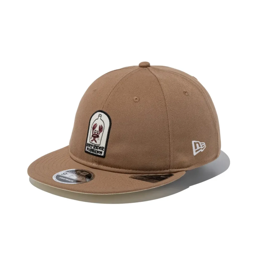 Tan flat brim snapback embroidered with a bottle and crab illustration representing the Surf Rider Foundation on the front panel