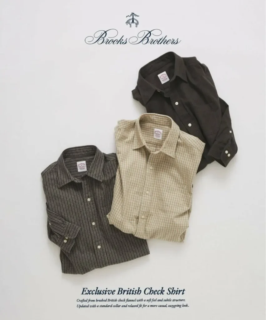 Three folded Brooks Brothers brushed British check flannel shirts arranged diagonally on a light gray backdrop. The collection includes a charcoal micro-check shirt, an olive-and-brown check shirt, and a beige plaid version, each displaying a classic point collar, button placket, and signature Brooks Brothers neck label