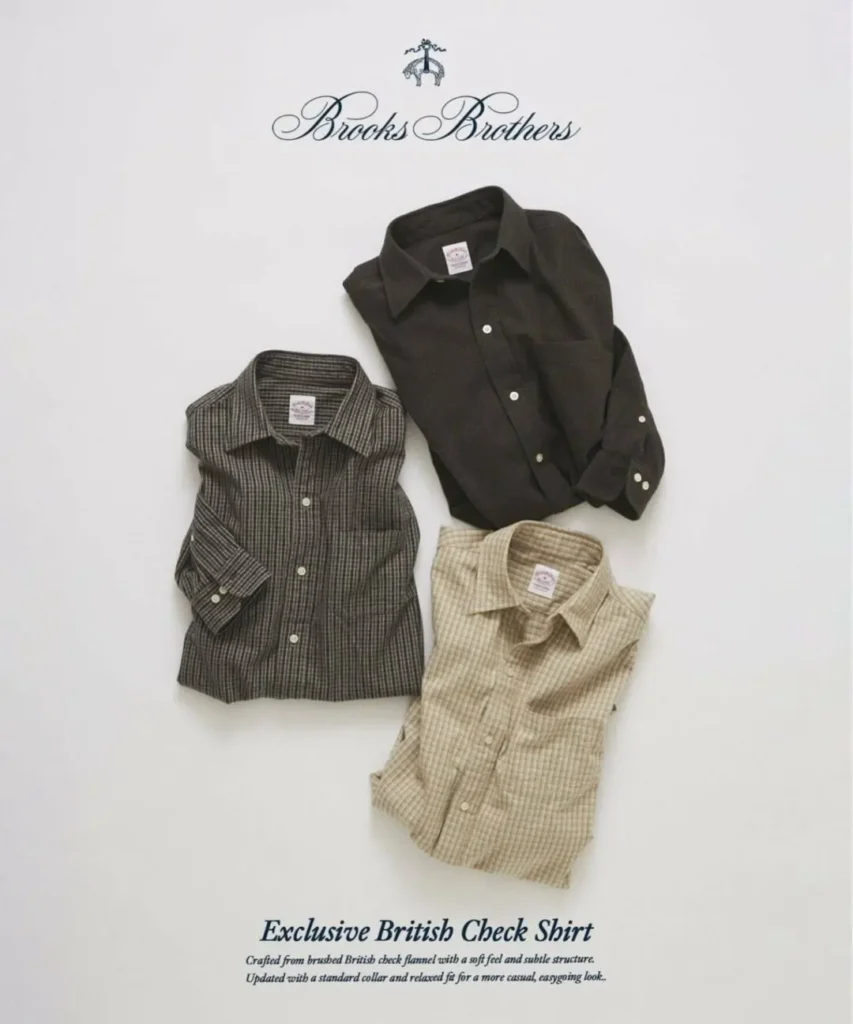 Flat-lay arrangement of three folded Brooks Brothers Exclusive British Check Shirts positioned in a triangular layout. The shirts feature soft brushed flannel construction, subtle British check patterns in charcoal, olive, and beige tones, with visible collars, button fronts, and woven brand labels against a minimalist background